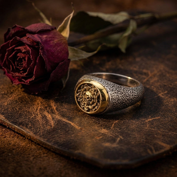 Lifestyle still life of the skull and rose ring resting on dark leather beside a dried red rose echoing the design