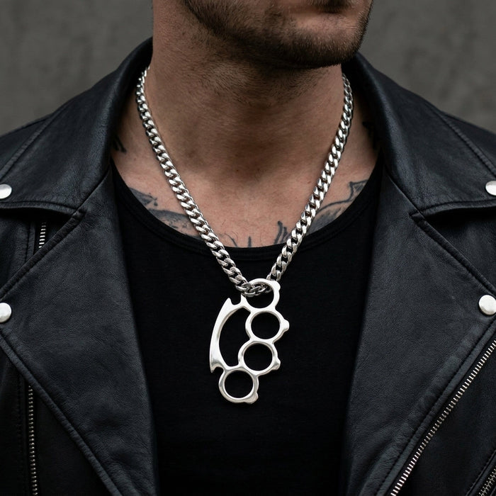 Sterling silver knuckle duster pendant on a thick Cuban-link chain, worn by a male model in a black leather jacket.