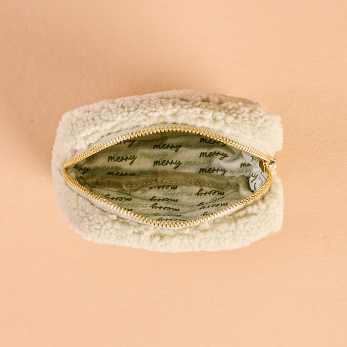 Top view of The Darling Effect's Square Holiday Gift Bow Green Teddy Pouch, featuring soft cream sherpa, a gold zipper, and light green lining with "merci" in black script. Ideal for fans of cozy holiday-themed Teddy Pouches.