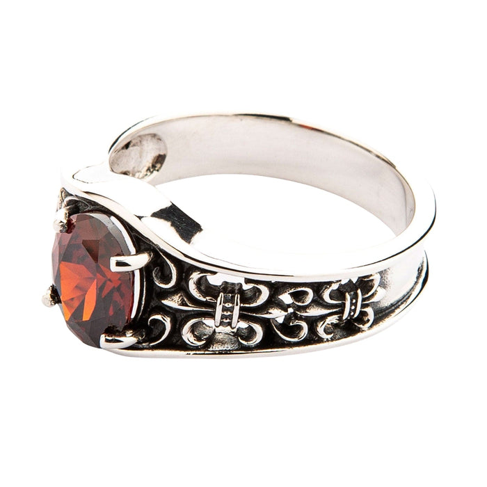 A gothic-style ring with a deep red garnet, showcasing the intricate Fleur de Lis pattern on the band.