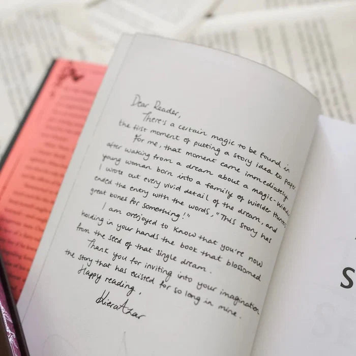 This image shows an open book with handwritten text on one of the pages. The handwritten note is addressed to a reader and expresses the author's joy and gratitude for the reader's interest in their book. The note mentions the magic and vivid detail of the story, and how it has blossomed in the reader's imagination. The handwriting is neat and legible, and the page is clean and well-preserved. The book appears to be a paperback with a red cover, and the page number "S" is visible in the bottom r