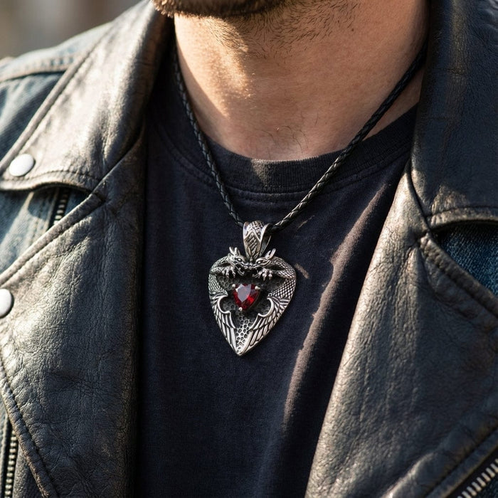 Close-up of a man wearing a sterling silver twin dragon pendant featuring a central red heart-shaped gemstone on a black braided leather cord, styled with a black t-shirt and leather biker jacket.
