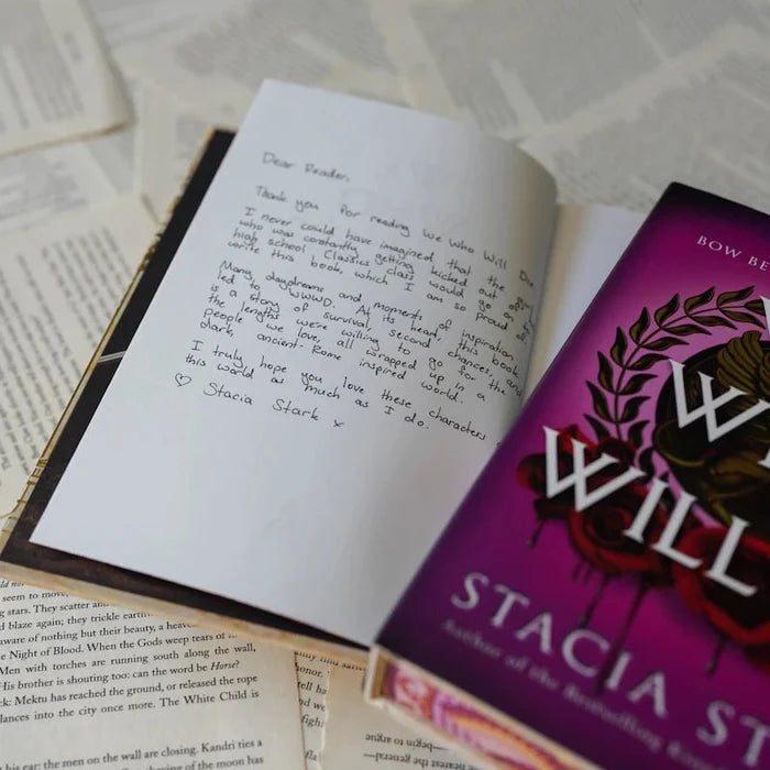 Exclusive handwritten Dear Reader author letter from Stacia Stark inside the We Who Will Die LitJoy Edition, signed with a heart, displayed open next to the purple book cover on scattered book pages