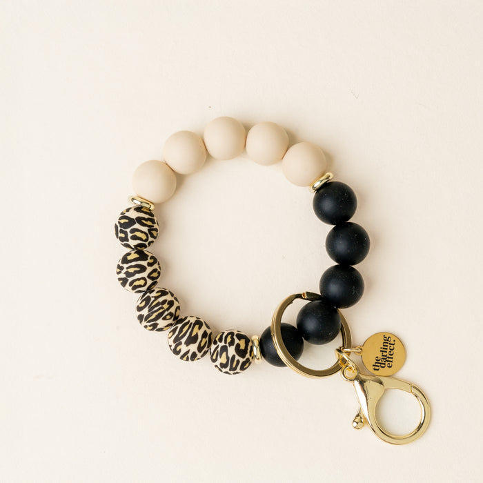 The-darling-effect’s Wild Child Hands-Free Keychain Wristlet features beige, black, and leopard print beads with a gold clasp and charm—a stylish, hands-free accessory for your keys.