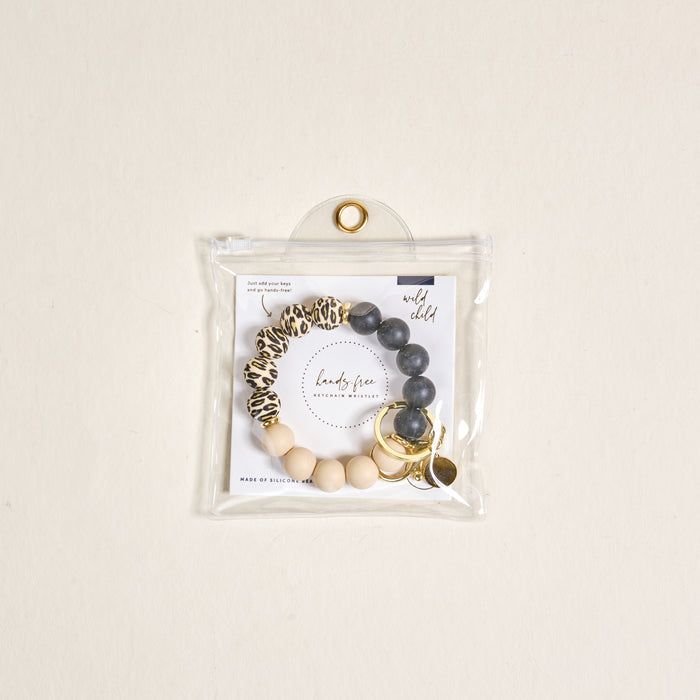 The Wild Child Hands-Free Keychain Wristlet by the-darling-effect features leopard print, dark gray, and beige silicone beads with gold key rings and charms, all in a clear button-closure pouch for chic, hands-free carrying.