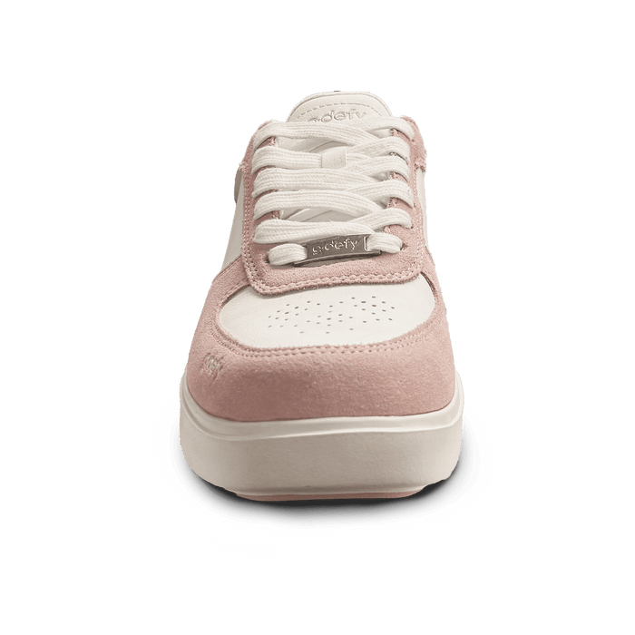 White and pink sneakers with white laces and pink suede accents, featuring a silver "defy" logo tag.