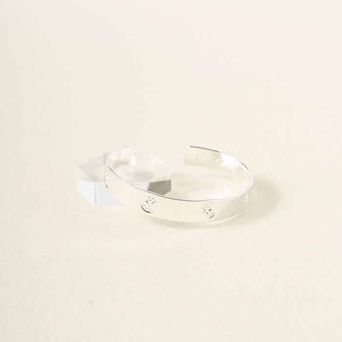 The Darling Effect's You Are Loving Cuff Bracelet in sterling silver, featuring subtle engravings, is shown on a light beige surface next to a clear geometric block—a thoughtful gift for any occasion.